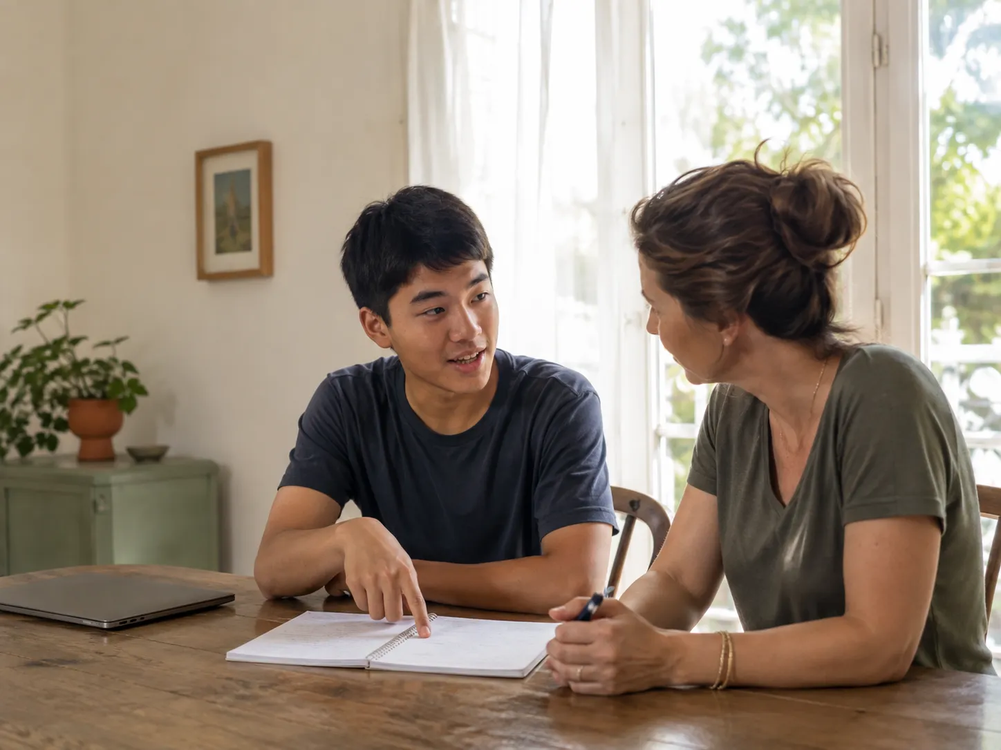A student talking through their notebook with a mentor at a table, the mentor listening.